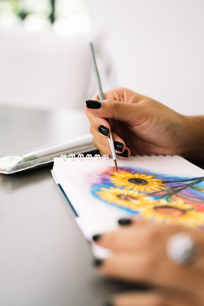 A hand paints vibrant sunflowers on a sketchpad, showcasing creativity and artistic expression.
